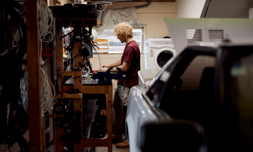 Isaac Grigor stands at a work station in his garage making a wooden chopping board. 