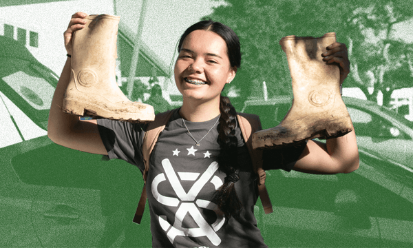 A high school volunteer wearing an SVA T-shirt holds up two gum boots and smiles.