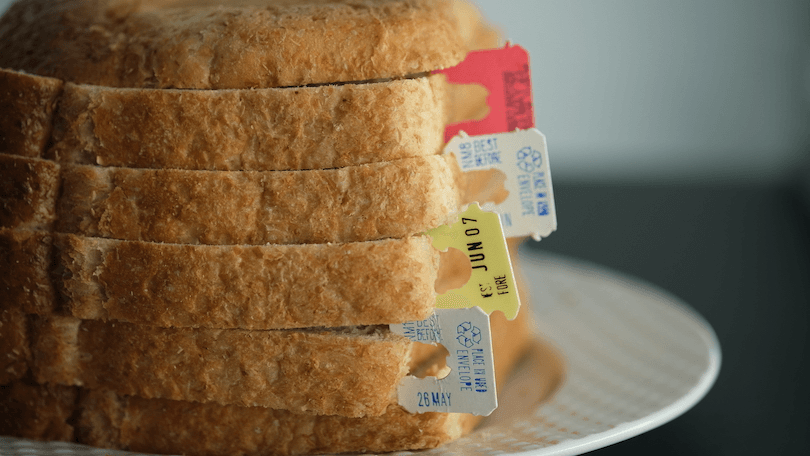 a stack of sliced bread with different bread tags featuring best before dates poking out from between the slices