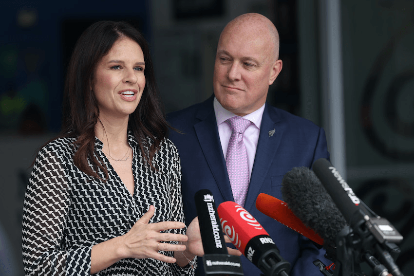 a woman in a polka dot dress and a man in a blue suit speak into microphones at a media stand up