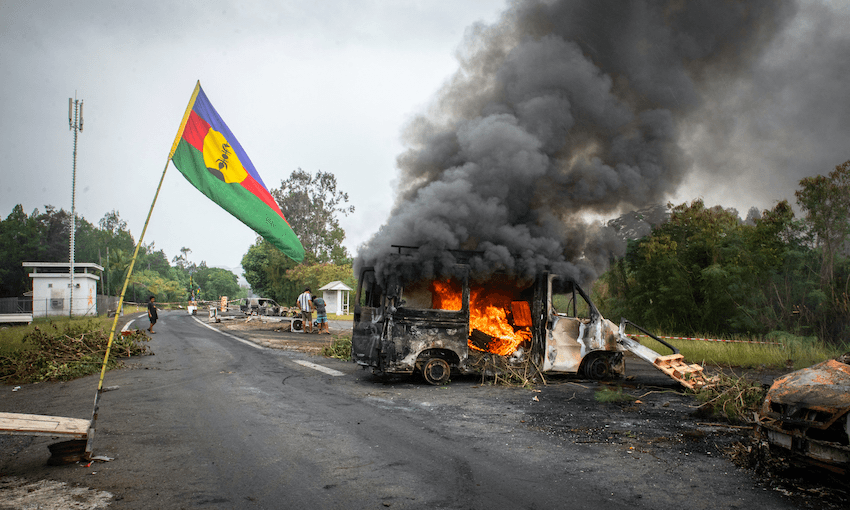 A Kanak flag flies next to a burning vehicle at a roadblock in La Tamoa, Paita, to the north of Nouméa (Photo: DELPHINE MAYEUR/AFP via Getty Images) 
