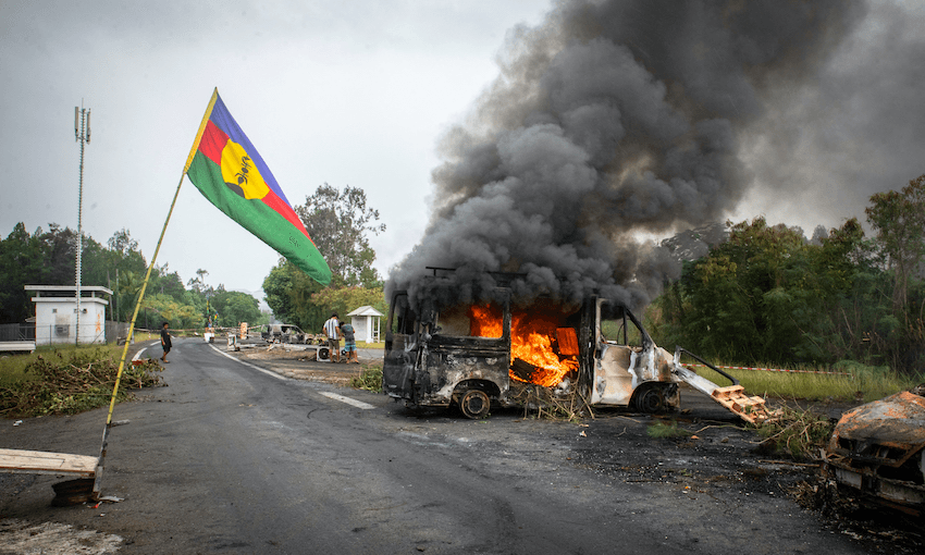 A Kanak flag flies next to a burning vehicle at a roadblock in La Tamoa, Paita, to the north of Nouméa (Photo: DELPHINE MAYEUR/AFP via Getty Images)