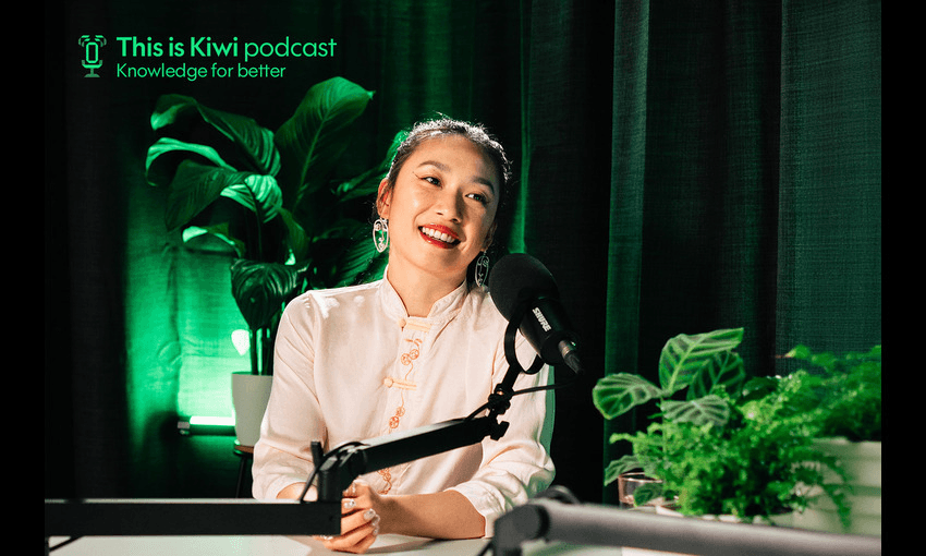 Jess Hong in a white blouse sits in front of a microphone, smiling. Behind her are green plants and a backdrop. Text on the backdrop reads, "This is Kiwi podcast - Knowledge for better.