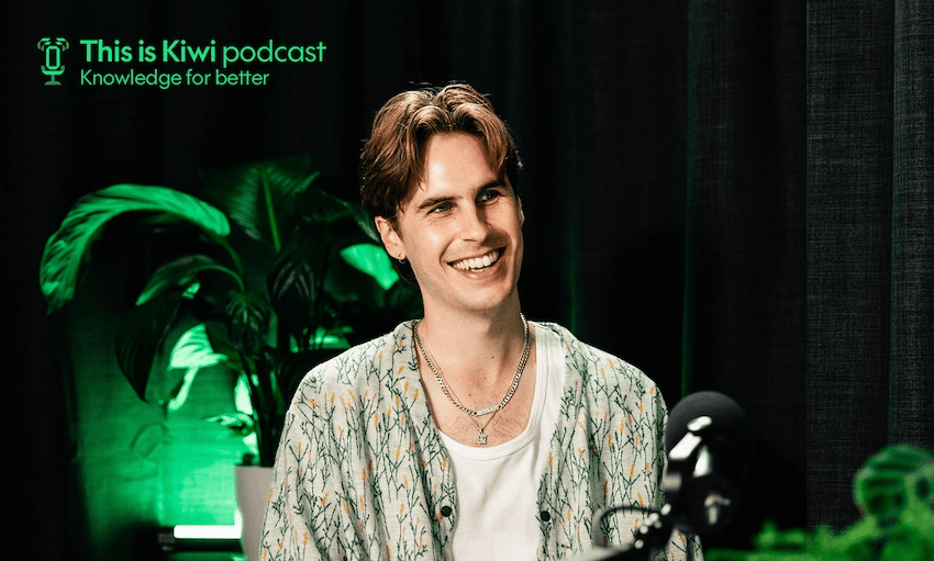 "A young man with light brown hair, wearing a patterned shirt over a white t-shirt and two necklaces, is smiling while seated in front of a microphone. Behind him, there are green plants and dark curtains. In the top left corner, the text reads 'This is Kiwi podcast, Knowledge for better' in green."