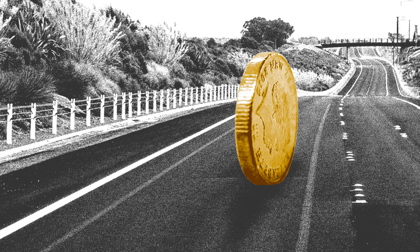 The image shows a large coin standing on its edge in the middle of a road. The background is a rural or semi-rural setting with trees and foliage on either side of the road. There is also a small bridge or overpass in the distance. The image has a black-and-white filter applied, except for the coin, which is in color, making it stand out prominently.