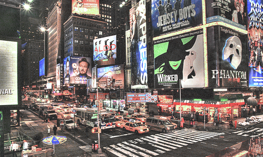 The image depicts Times Square in New York City at night. It is filled with bright lights, large billboards, and advertisements. Several notable signs include those for "Wicked," "The Phantom of the Opera," "Jersey Boys," "Rock of Ages," "Conan O'Brien," and "Express." The streets are bustling with yellow taxis, cars, and pedestrians, capturing the vibrant, busy atmosphere of this iconic location.