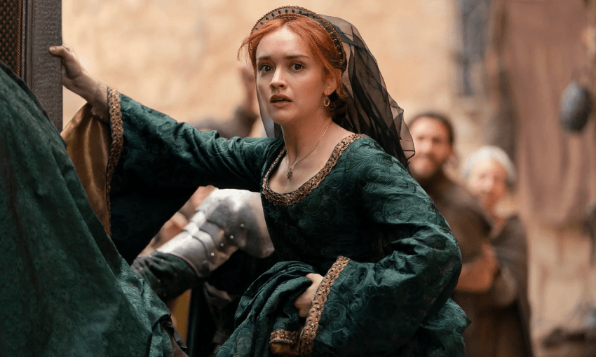 A woman (Olivia Cooke as Alicent Hightower) with red hair, dressed in an elaborate green medieval-style gown with gold trim, looks determined and slightly distressed. She is climbing into a carriage.