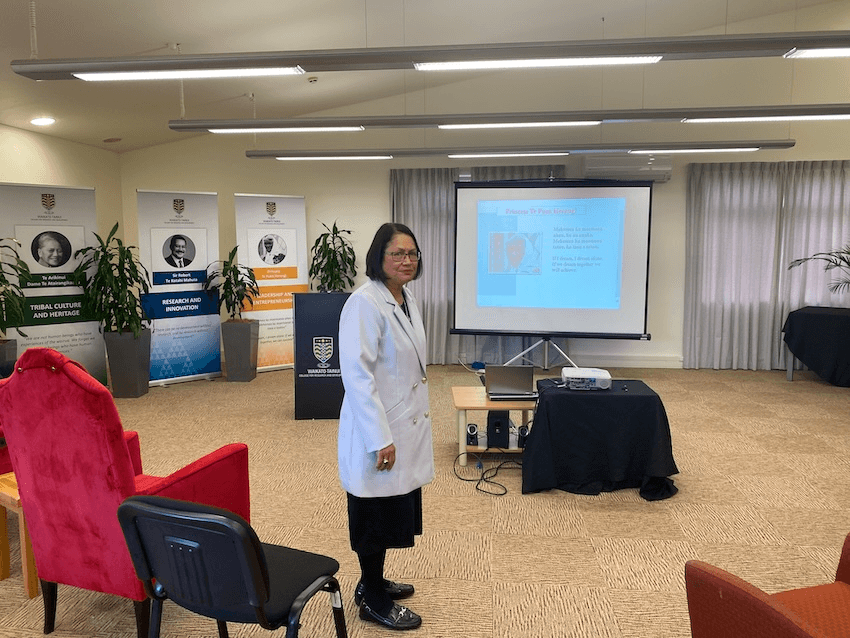 a māori woman standing in a conferance room wearing a white coat 