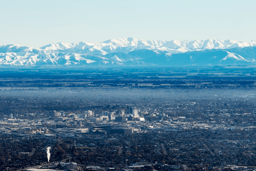 the city of chrsitchurch with sparkly alpine mountains in the background and and a miasma of fog poised over the centre city