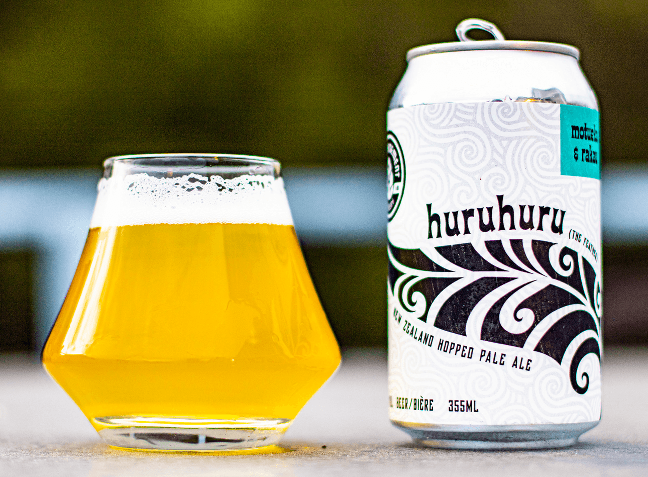 A glass of beer next to a white can with a black silver fern and the word "huruhuru" written on it.