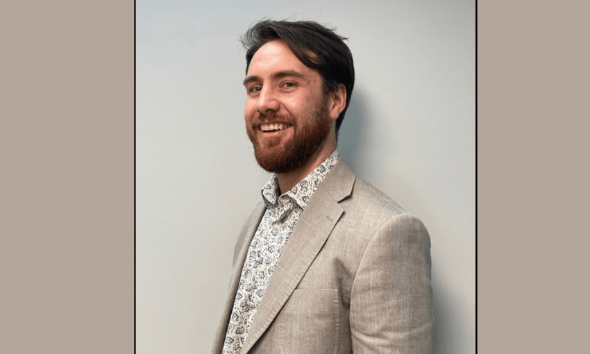 a beige background with a smiling white man with a dark brown beard and hair and a textured linen blazer