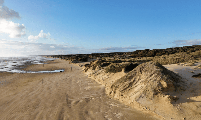 Silhouette of various human figures walking along Te Oneroa-a-Tōhe. The oceran is to the left of the frame and sand dunes to the right, which are covered in some greenery.