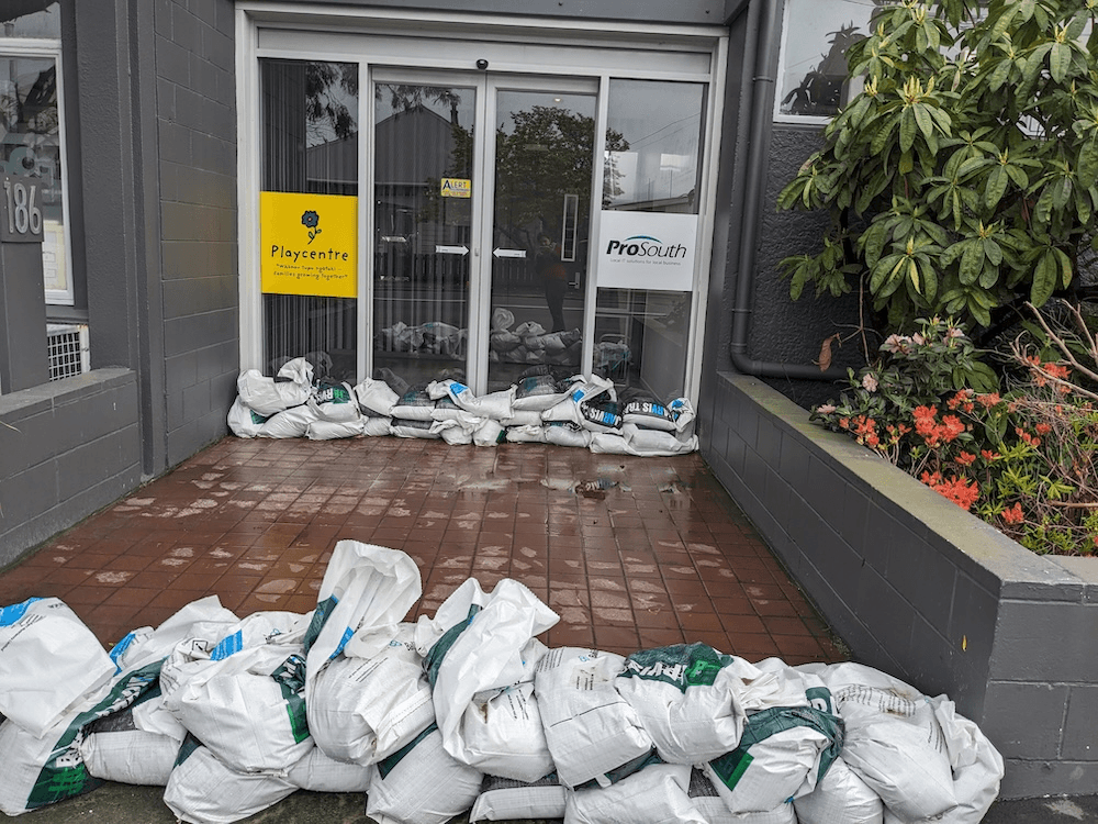 lots of sandbags in front of a playcentre in South Dunedin. if you look closely you can see the journalist wearing blue jeans and a red jacket in the reflection of the glass, which she did not realise until uploading the image just now