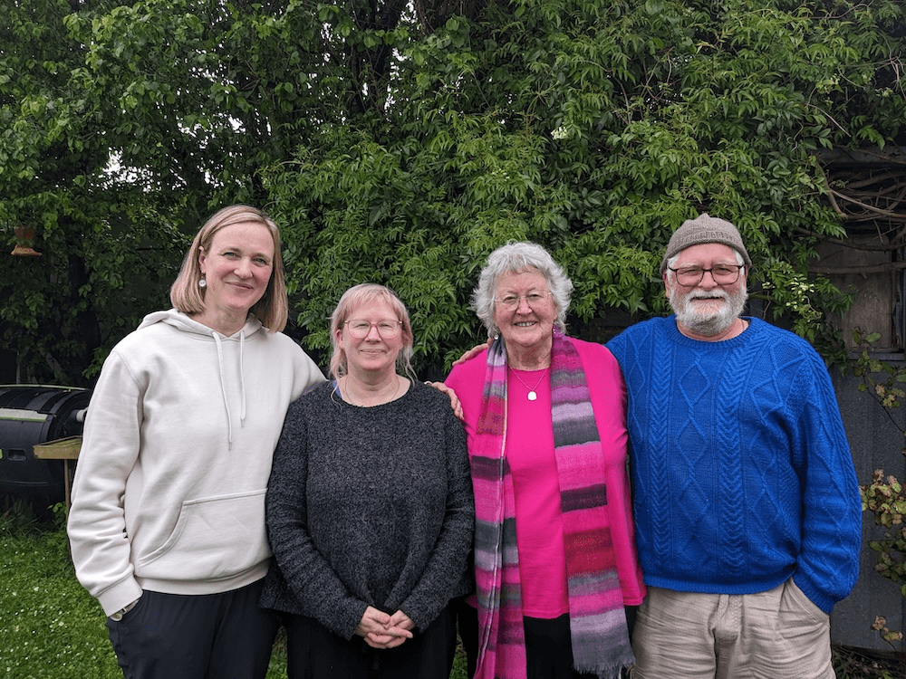 a green backyard background with four white people of various ages standing in a row