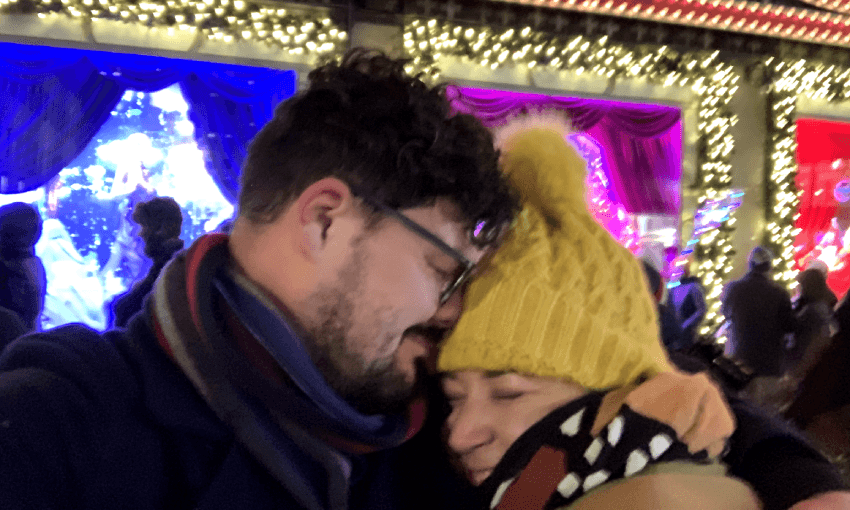 A couple embraces warmly in front of a festive store window.