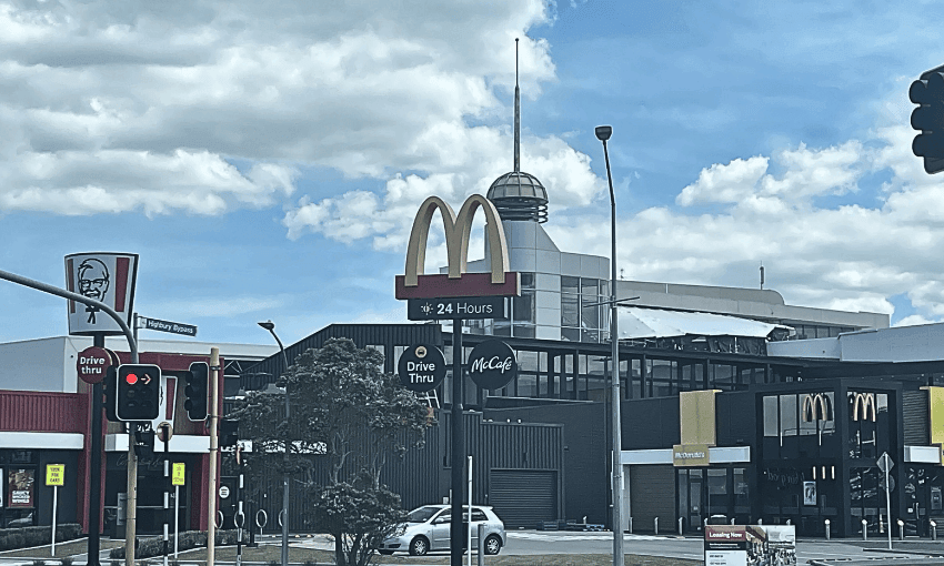 A McDonald's restaurant with a large golden arches sign and a "24 Hours" label. The establishment features a McCafé and a KFC drive-thru nearby. The sky is partly cloudy. The Highbury mall is in the background