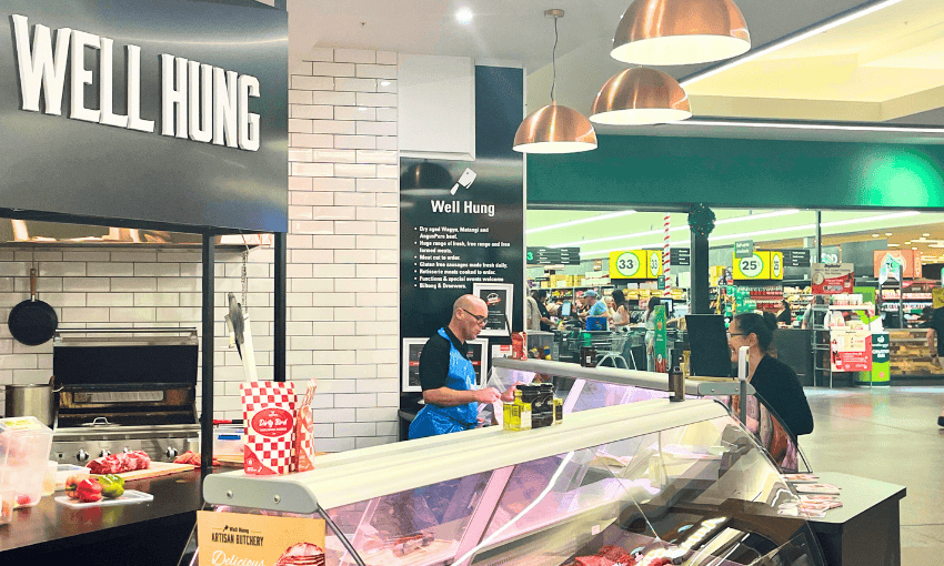 A butcher in a blue apron serves a customer at the "Well Hung" meat counter in the milford shopping centre