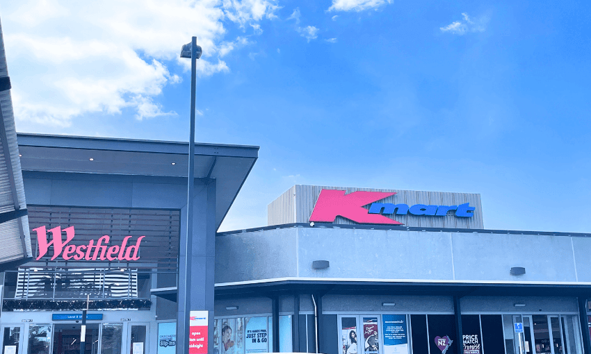 A shopping center with a Westfield entrance on the left and a Kmart store on the right under a clear blue sky.