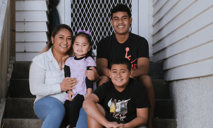 A family sits on the front porch steps of their home. The mother is smiling wearing a white top and blue jeans. Her primary school aged daughter sits on her knee wearing a purple dress and bow and her two older brother both in black t shirts are sitting beside them.