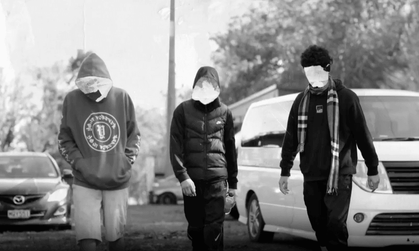 Three people with pixelated faces walk down a street. The person on the left wears a hoodie and shorts, the middle person wears a puffer vest, and the person on the right wears a scarf. A white van and car are parked beside them. The image is in black and white.