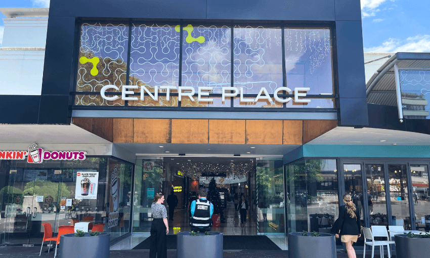 The image shows the entrance to a shopping center named "Centre Place," with a modern dark facade. There are people walking in and out, and a Dunkin' Donuts shop is visible on the left.