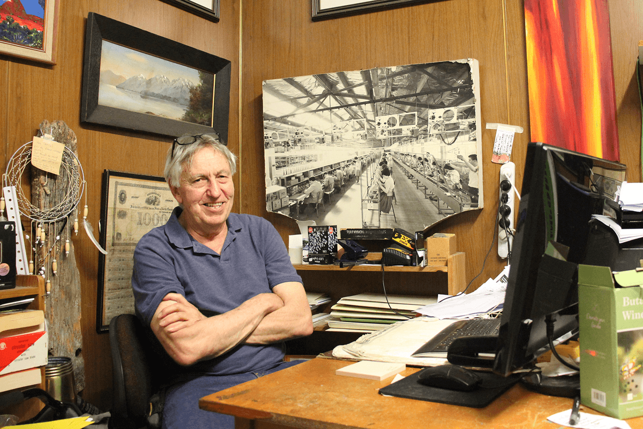 Photo of an older man sitting at.a desk with paintings, photos and trinkets around him