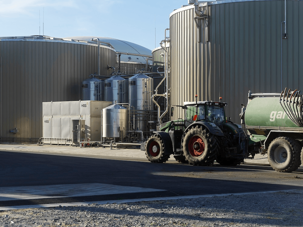 a small tractor in front of a huce cylindrical tank on a sunny day gives a sense of just how much volume 75 thousand tonnes of food waste is