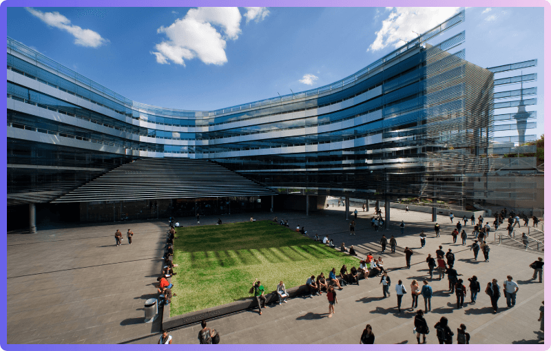 Sir Owen G. Glenn Building: A wide-angle view of the Sir Owen G. Glenn Building, showcasing its modern glass facade and the courtyard with people gathered and walking.