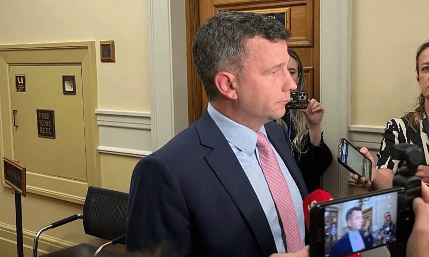 David Seymour wears a suit and pink tie while speaking to reporters in the hallway at parliament. he looks off screen 