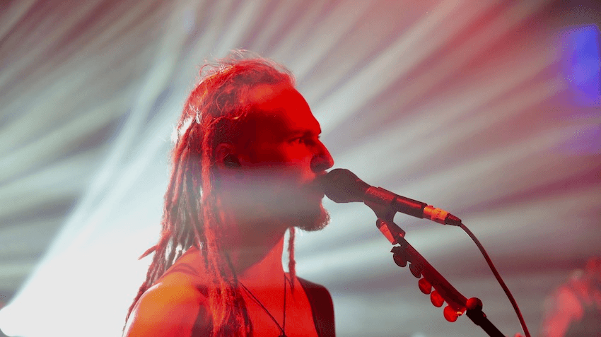 A man with dreadlocks sings into the microphone on stage