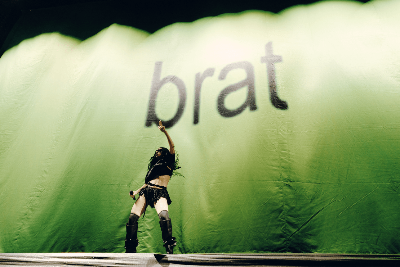 Charli XCX in front of a bright greet banner with "brat"