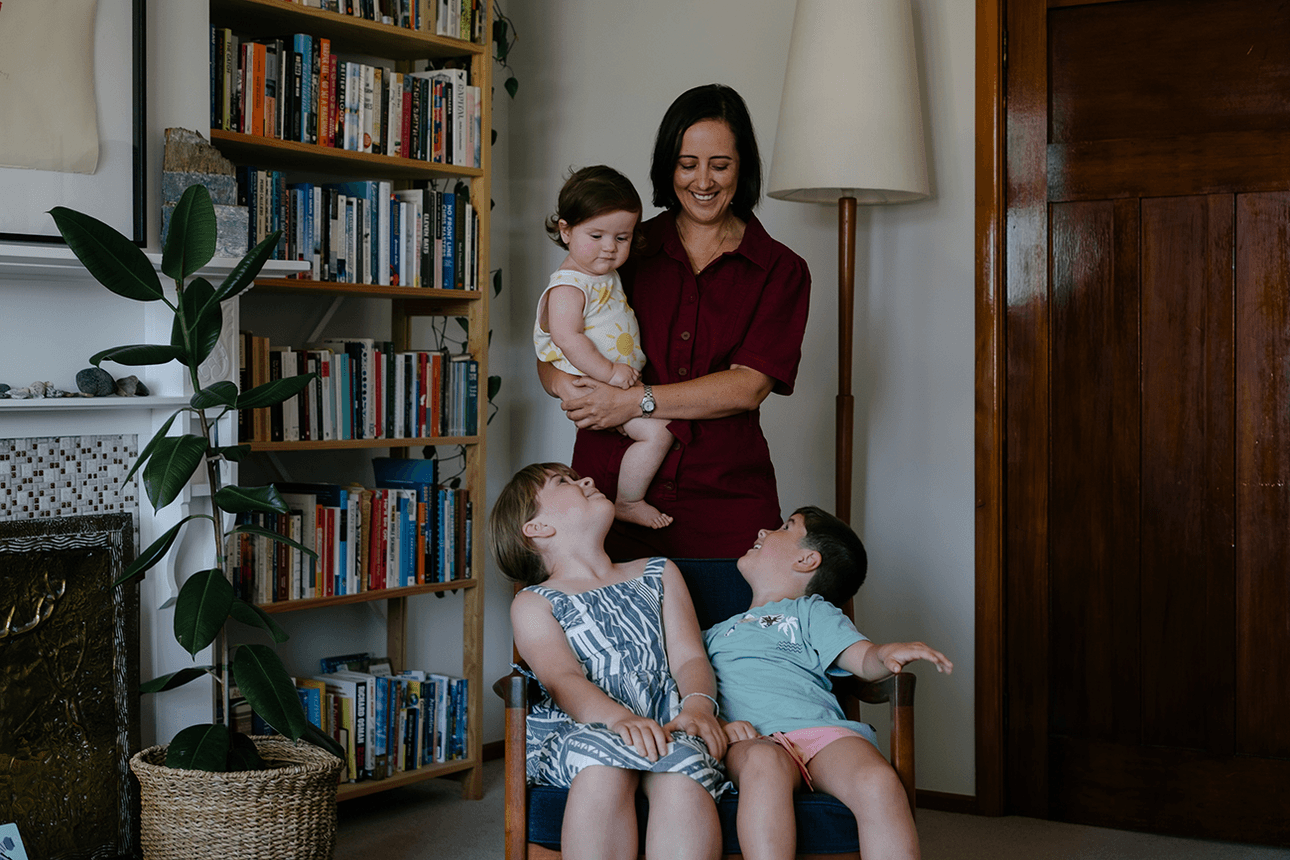 photo of woman in a red dress holding a baby with two other small children. bookshelf behind them