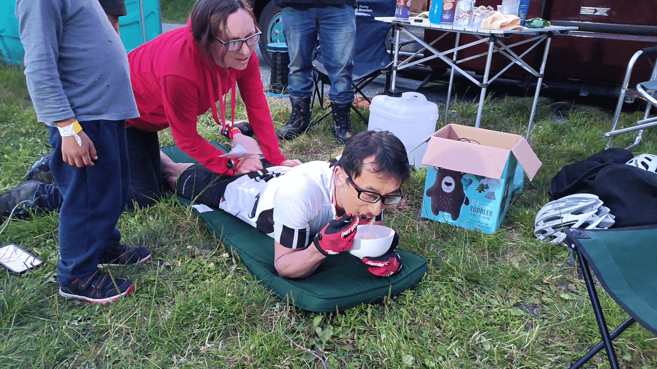 Ken Looi lying down on a cushion during his world record attempt. He is heading a bowl of noodles and his wife is giving him a massage. 