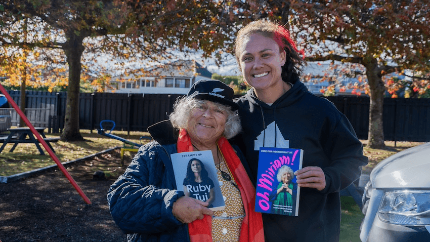 Miriam Margolyes and Ruby Tui smile at the camera, each holding a copy of the other's memoir