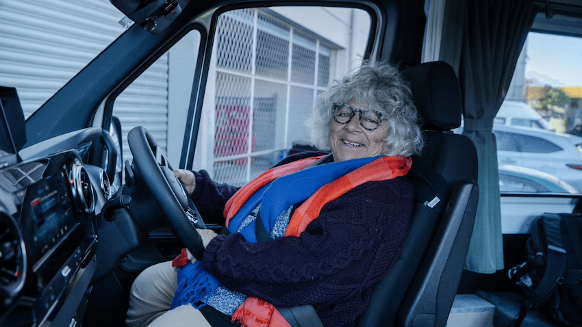 Miriam Margolyes sits in her campervan and smiles at the camera