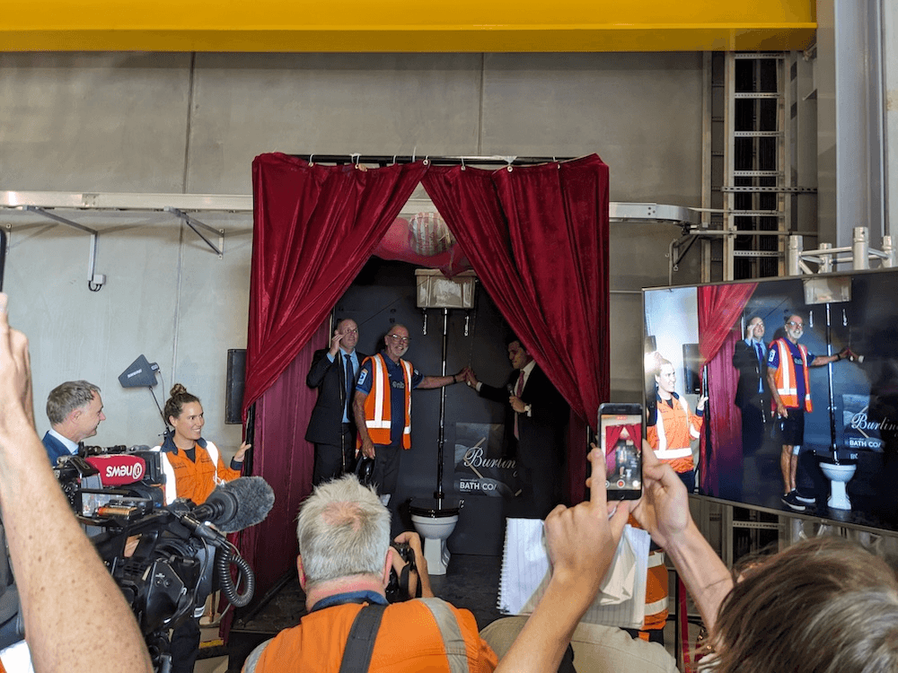 three people, surrounded by a crown, flush a toilet surrounded by a big velvet curtain