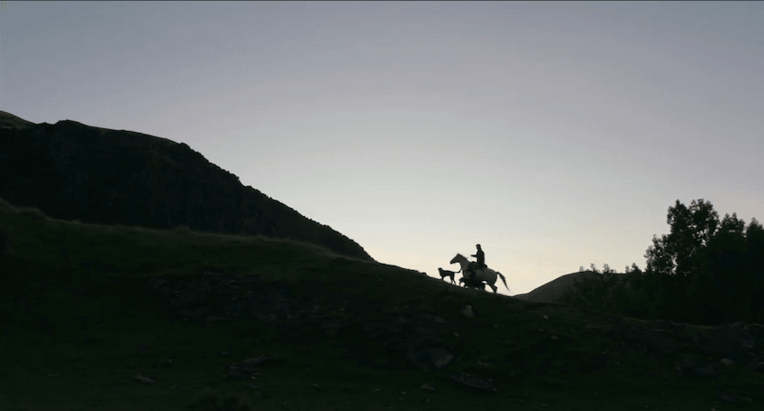 A farmer rides a horse along a farm ridge at sunrise