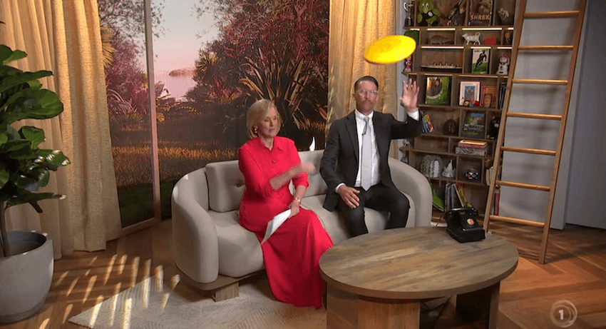 Hilary Barry and Jeremy Wells sit on a couch in the Seven Sharp studio, as Jeremy catches a yellow frisbee flying in the air