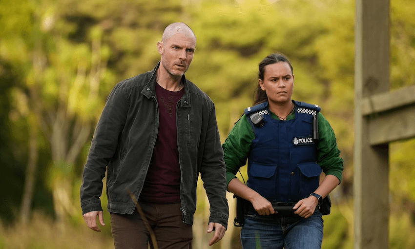 A man wearing a black jacket and a woman wearing a blue police vest walk together in a scene from NZ TV drama The Gone