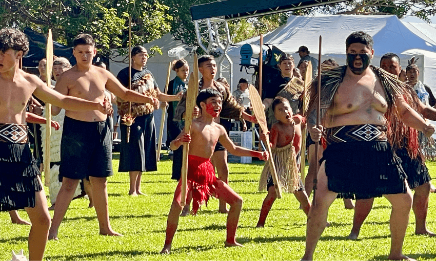 A group of people, including children, perform a traditional haka dance outdoors at the Upper Treaty Grounds at Waitangi.