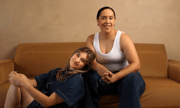 brynley stent and kura forrester, hosts of bryn & ku's singles club, sit together on a brown sofa