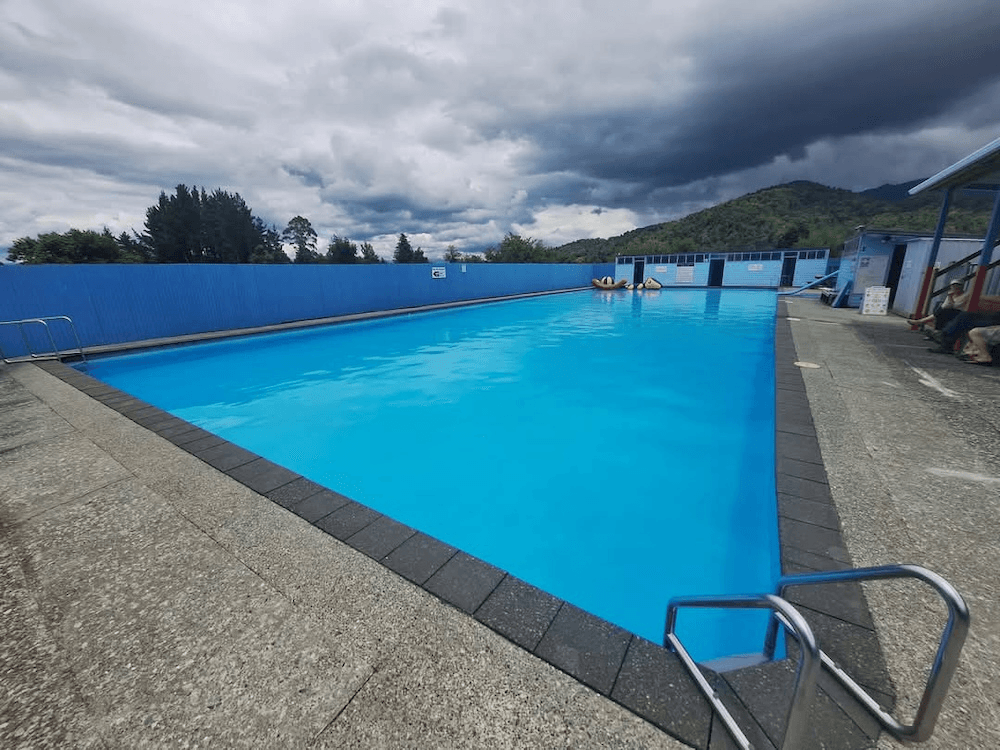 a regtangular pool, bright blue underneat brooding stormclouds and the dark texture of hills