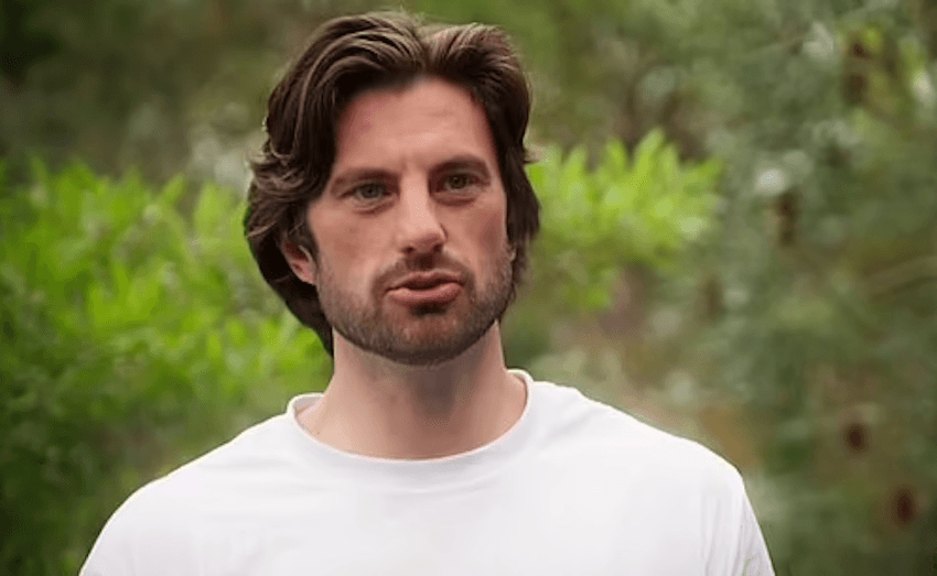 A European man in his mid-30s addresses the camera in a white tshirt