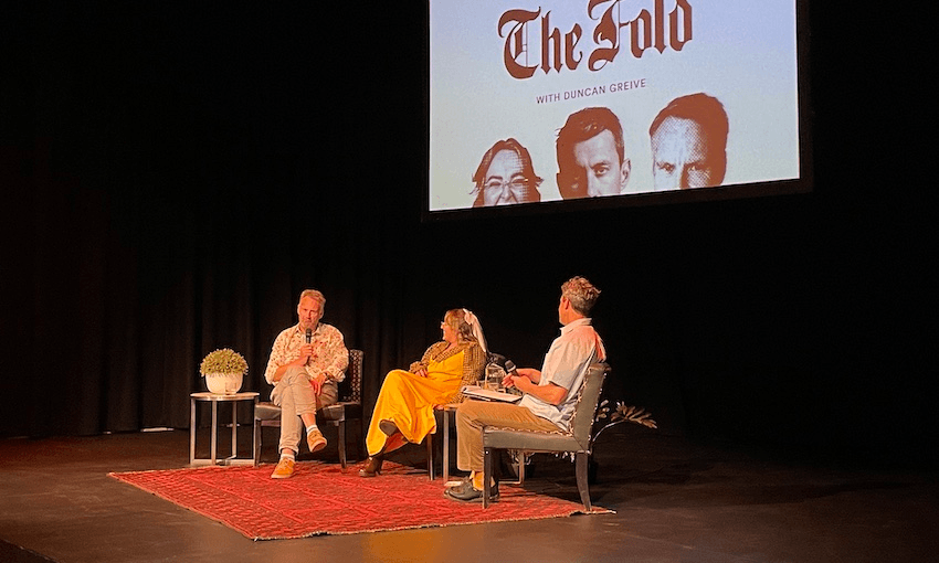 three people sitting on chairs on a stage with a red rug and a backdrop that reads 'the fold'