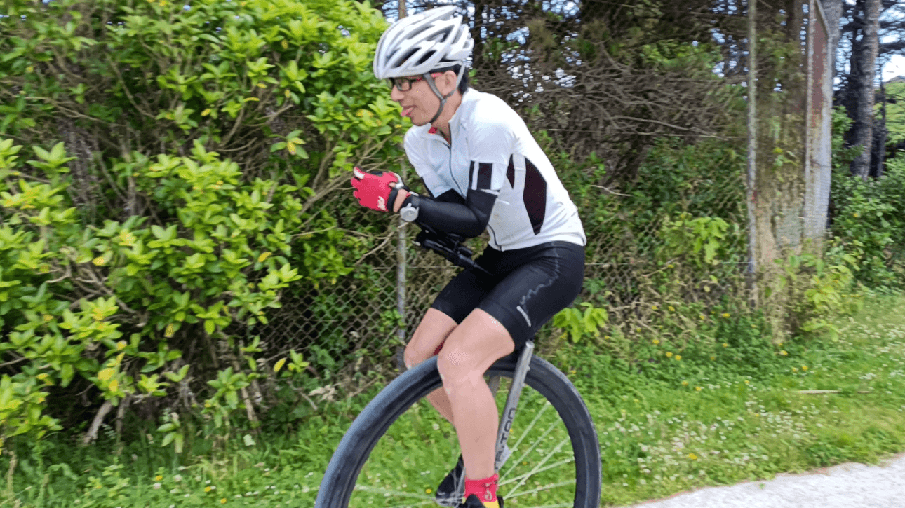 Ken Looi riding his unicycle at Newlands Intermediate during his world record attempt. There are trees in the background. He is poking his tongue out. 