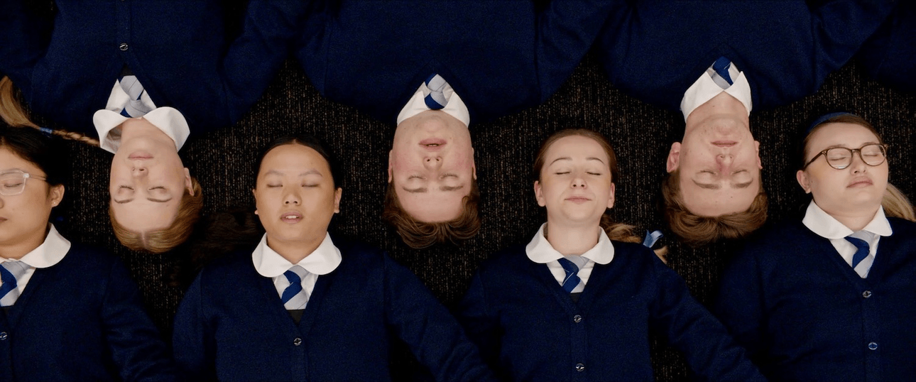 A still from Tinā showing seven school students lying down with their heads alongside each other
