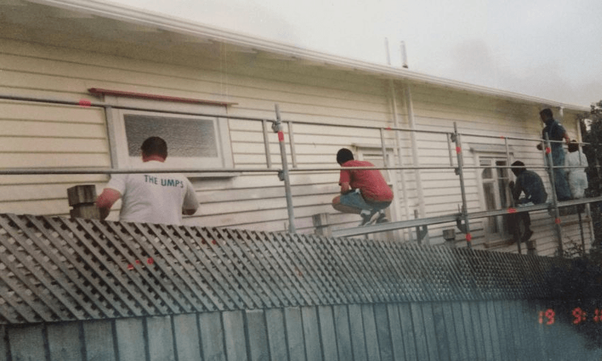 An old photo of five adult films painting the side of a house during a large scaffolding