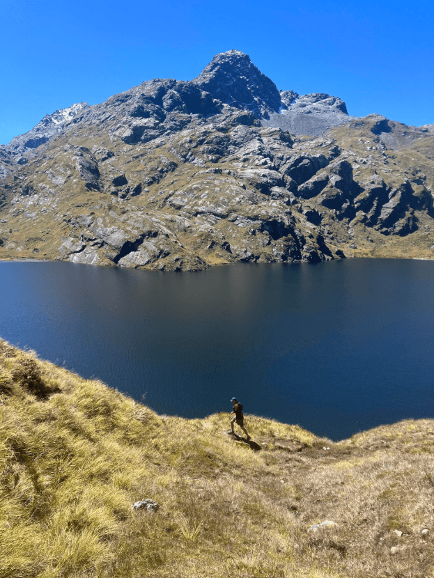 a mountain and lake with small figure hiking along the trail