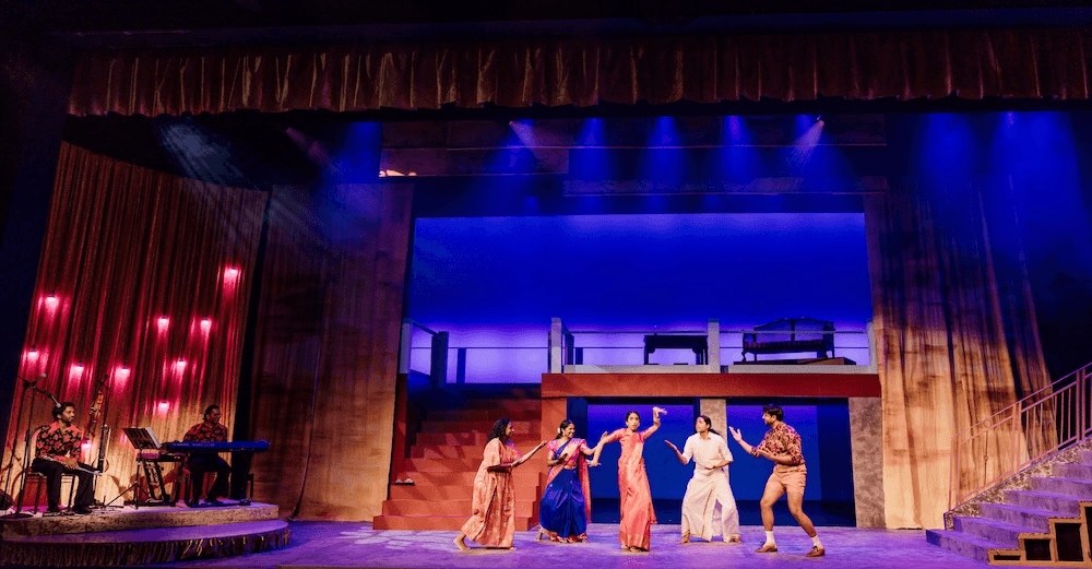 blue stage lights and a house set up with five characters in different colourful outfits dancing together