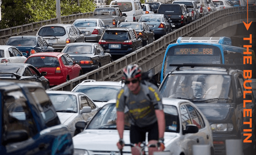 Heavy traffic on a multi-lane road with numerous cars and a blue bus. In the foreground, a cyclist in a helmet and sunglasses rides along the congested road. The words "The Bulletin" are on the right side in orange text.